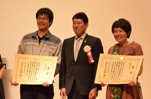 受賞した２人と笑顔で記念撮影する文部科学大臣政務官の樋口尚也氏。